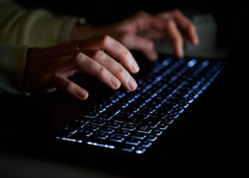 Hands of anonymous person typing on laptop keyboard at night, close up. Cyber security concept