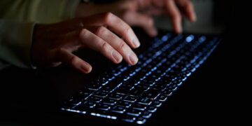 Hands of anonymous person typing on laptop keyboard at night, close up. Cyber security concept